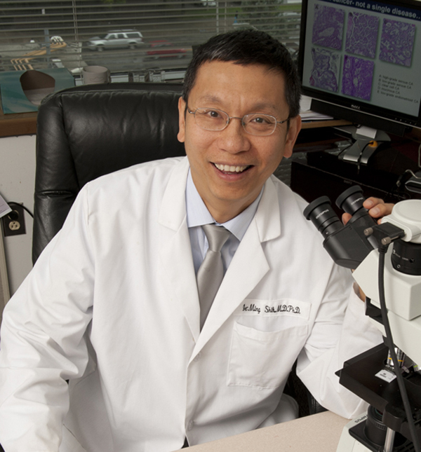 Ie-Ming Shih, MD, PhD, smiling in research lab, holding microscope