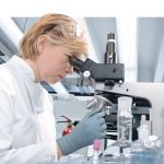 researcher in lab coat looking through microscope