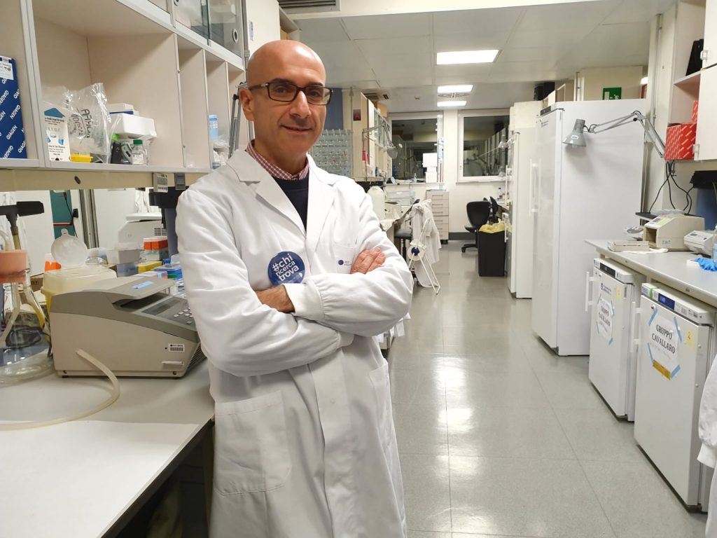 Dr. Ugo Cavallaro in research lab with arms folded, wearing lab coat, surrounded by lab equipment