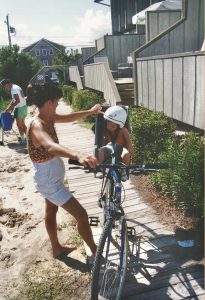 Andrew as a child, wearing a helmet on a bike while his mother stands next to him