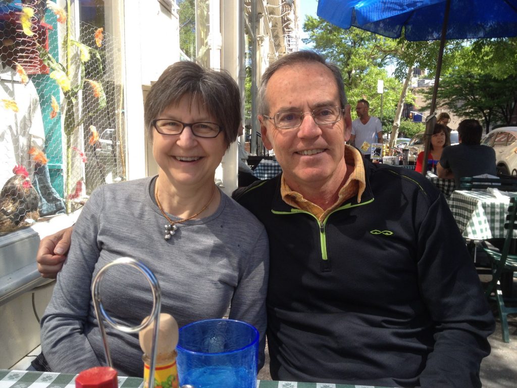 Jackie and Dennis seated outdoors at a restaurant. Dennis has his arm around Jackie and both are smiling. 