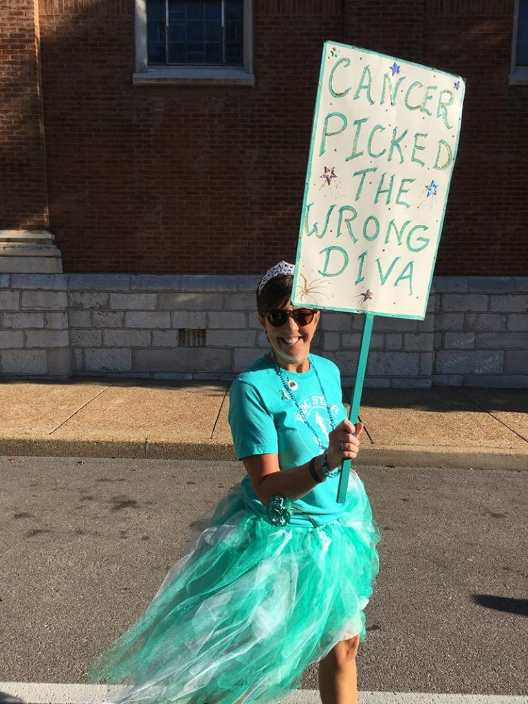 Sandy Sullivan wearing teal outfit and tutu and holding sign that says, cancer picked the wrong diva