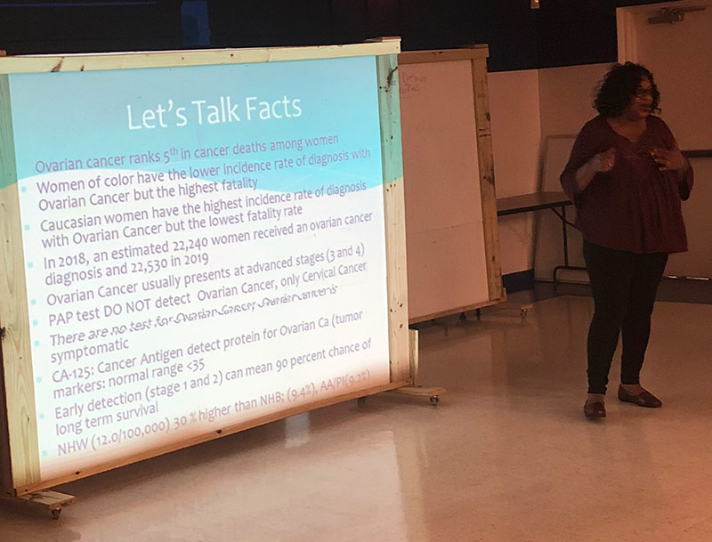 Yvette giving presentation next to a large screen reading, Let's talk facts, along with facts about ovarian cancer