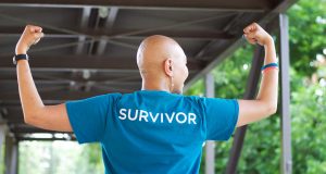 ovarian cancer survivor wearing teal survivor shirt, raising arms to show strength