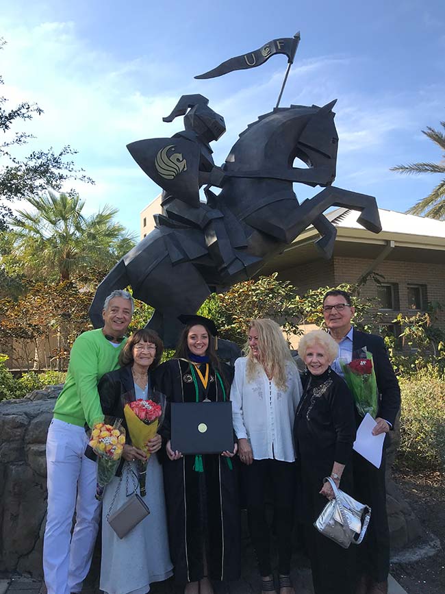 Dr. Gitto wearing cap and gown, posing with family in front of sculpture