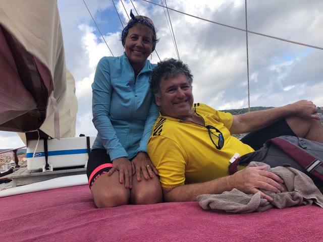 Penny with her husband, seated on a boat with the sky visible behind them, smiling