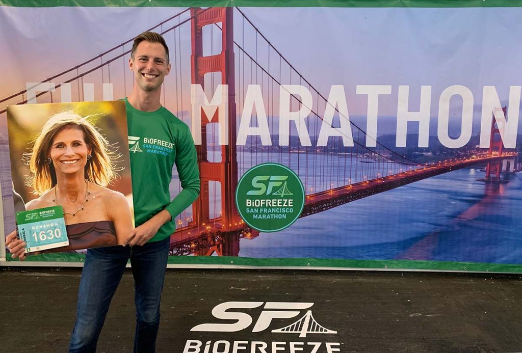 Jonathan smiling and standing in front of Marathon sign, holding photo of his mother