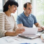 Couple at desk holding papers and looking at laptop together