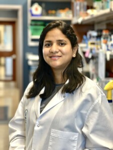Sonam Mittal smiling, wearing lab coat, in research lab