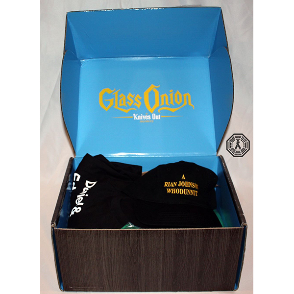 Box that reads Glass Onion Knives Out, containing black hat and shirt; hat reads a Rian Johnson Whodunit