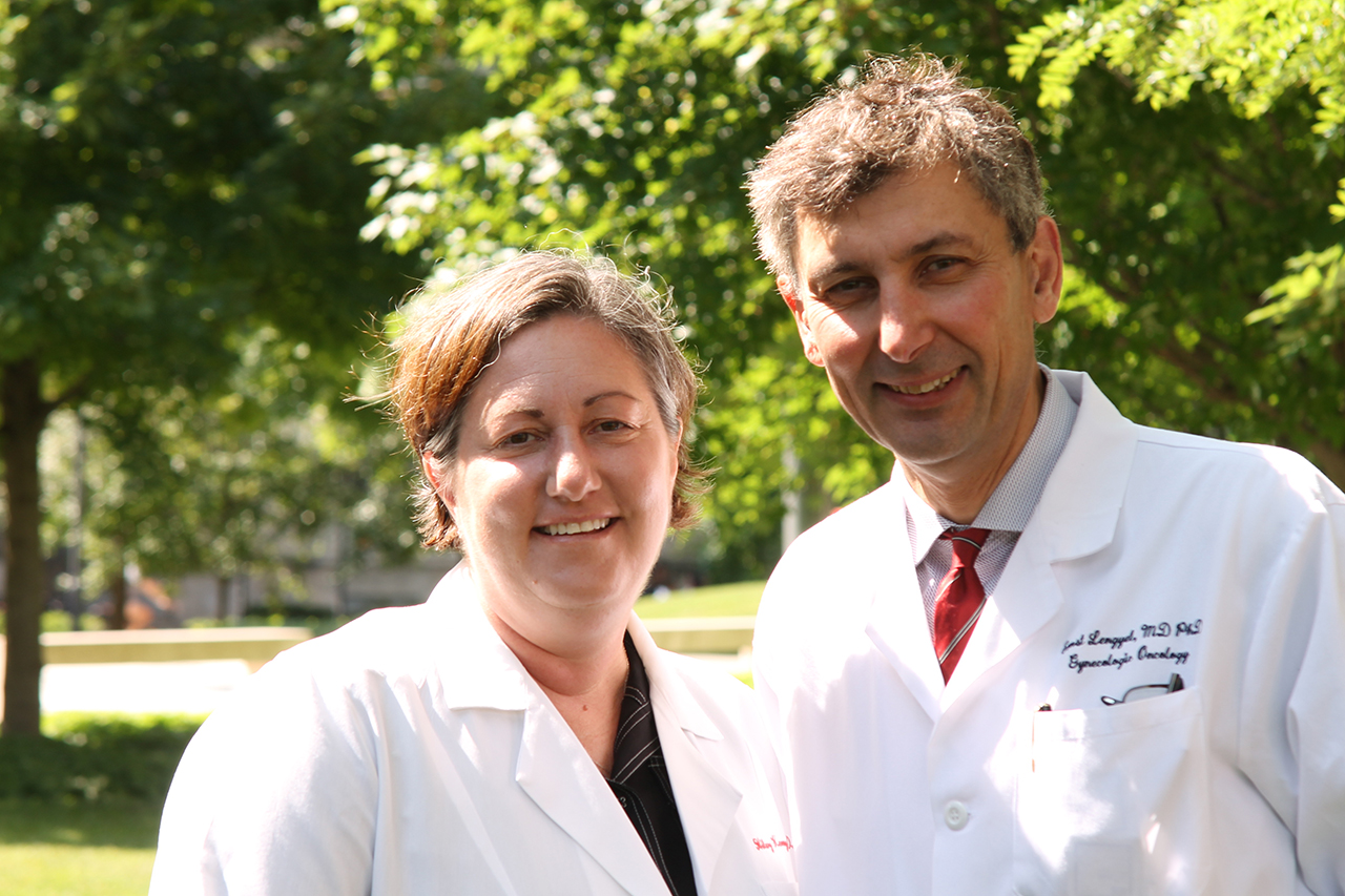 Dr. Hilary Kenny and Dr. Ernst Lengyel, both wearing white lab coats, standing together outside on a sunny day
