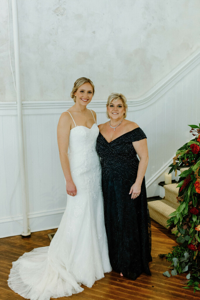 Sam and her mother on Sam's wedding day. Sam is wearing a long white wedding gown, and her mother is wearing an off-the-shoulder black dress. Both are smiling for the camera.