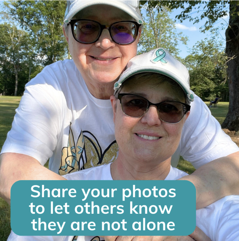 Photo with text: Two women at a park wearing white baseball caps with teal ribbons on the front, posing together and smiling for the camera. White text on teal background reads Share your photos to let others know they are not alone.