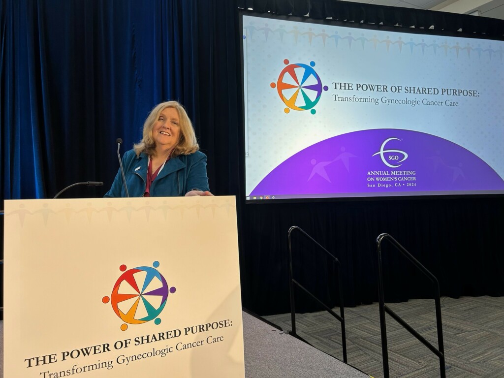 Photo: Susan Leighton stands at podium with banner reading The Power of Shared Purpose: Transforming Gynecologic Cancer Care