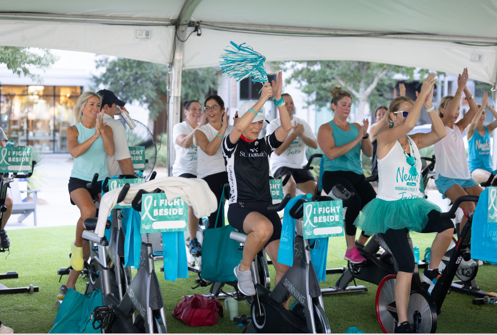 Happy people riding stationary bikes outdoors, smiling and clapping hands