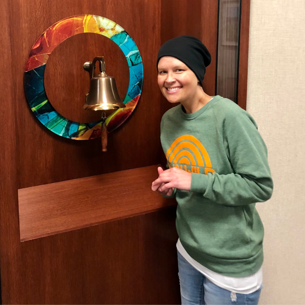 Woman in head wrap stands next to bell, smiling