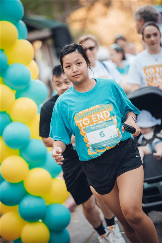 A runner toward front of the pack, wearing a teal shirt, passes teal and yellow balloons at the 2024 SummeRun.