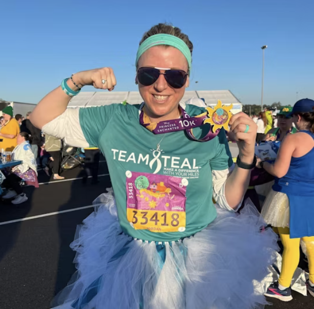 Woman wearing Team Teal shirt and teal headband makes victory sign