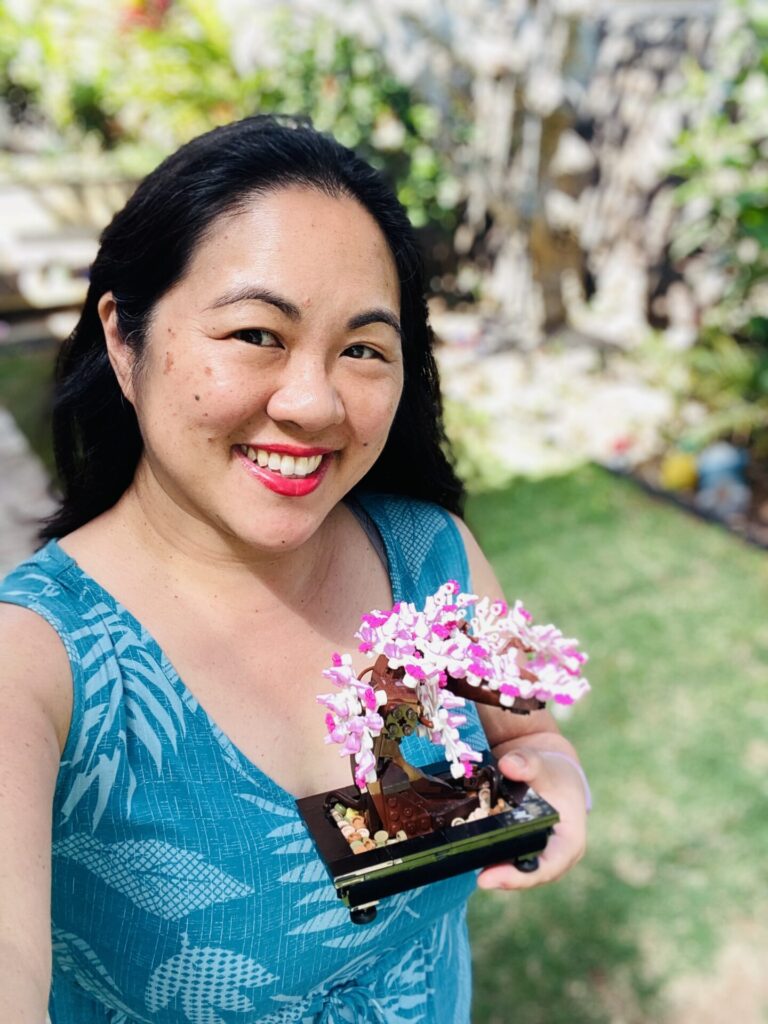 Woman standing outside in green grass, smiling and holding pink flowers